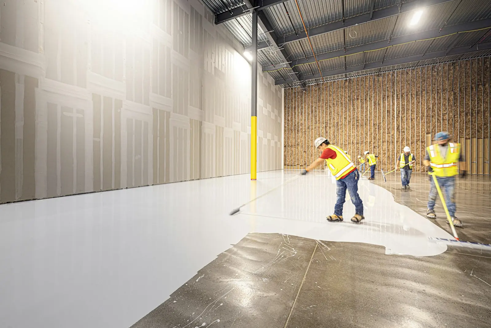 Crew applying a white floor coating across a commercial warehouse
